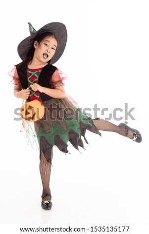 Halloween kids concept, portrait of little Asian girl in Halloween witch costume and black hat with pumpkin and broom on white isolated background, adorable cute young kid acting to be witch in studio