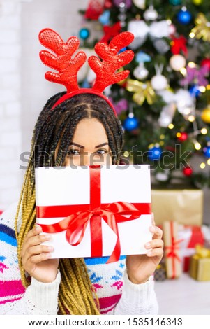 Young african american woman receive a Christmas gift. Happy excited dreaming girl about New Year presents. Christmas Eve, winter holiday decoration. Xmas celebration. Selective focus. Female at home