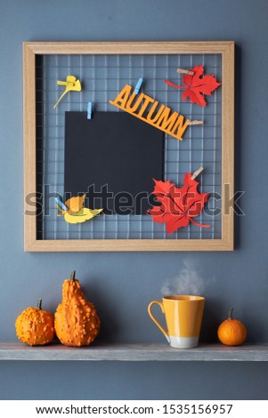 Photo grid board with red and orange paper Autumn leaves and text "Autumn". Cup of tea and Autumn decorations on a shelf. Fall-related mockup for your lettering, calligraphy, picture or drawing. 