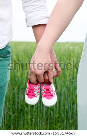 A woman and a man hold baby's shoes. A woman and a man are holding children's shoes in the meadow outdoors.  Expecting a baby conceptual picture. Family love.  