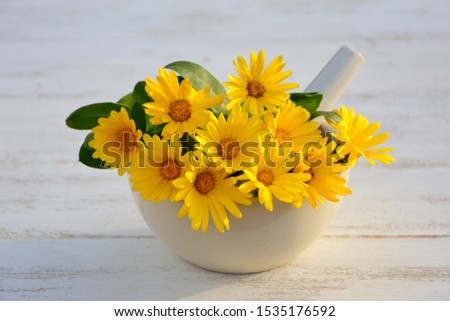 Calendula flowers in mortar on white wooden background close up