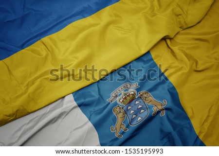 waving colorful flag of canary islands and national flag of ukraine. macro