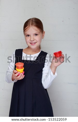Happy little girl in school uniform holding a tube of paint for painting on Education