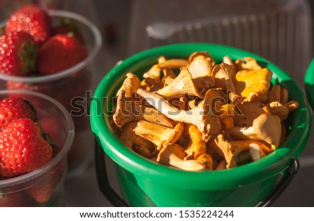 ripe chanterelle mushrooms in a green bucket next to ripe strawberries in a glass on the organic market