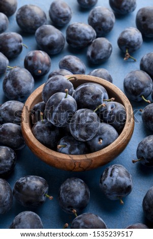 Plums on old blue table in wooden jar close up colorful arrangement with selective focus overhead studio shot