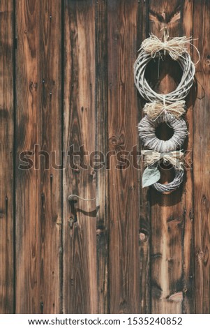 Decoration on a country house door. Photo of an old wooden door in a farmhouse. A white wicker ornament hangs on the door. Three white wicker circles.