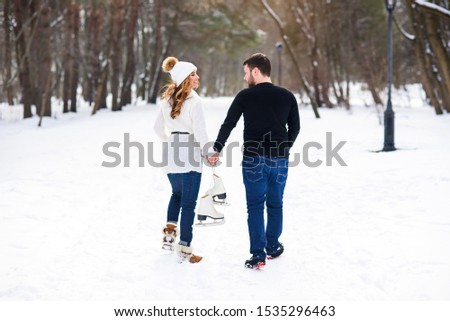 Close up loving couple walking on a date in a winter Park. Young man and his girlfriend holds each other to the hands and holding ice skates.