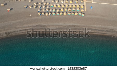 Aerial drone top down photo of organised with sun-beds and umbrellas black sandy beach of Kamari with deep turquoise sea, Santorini island, Cyclades, Greece