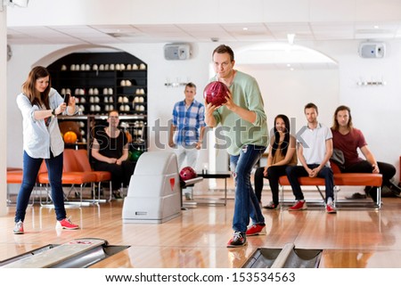 Young man bowling with female friend photographing at club