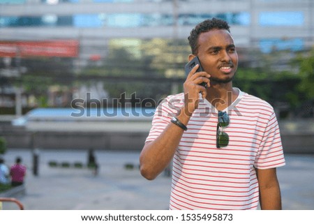 Happy young African bearded man talking on the phone in the city