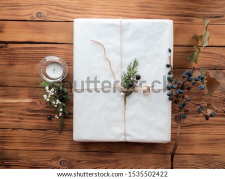 Top view of a large gift in white packaging with Christmas decor, a candle on a wooden background