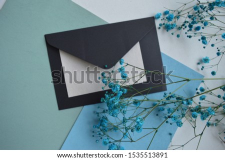 Black envelope and flowers, blue background, top view flat shot