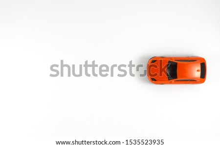 A red toy car on the white background in the top view which starts from the right hand of the picture