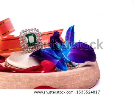 Closeup of Emerald ring on oyster shells with blue orchid flower and rose petals on white background. Jewellery gift concept with copy space