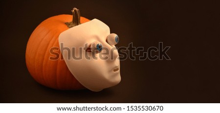 Halloween pumpkin with eyes dark banner stock images. Halloween pumpkin with eyes and scary mask. Creepy halloween pumpkin photo. Plastic human mask on pumpkin. Halloween plastic white face mask