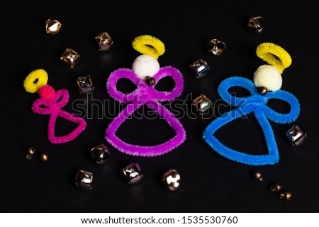 3 pipe-cleaner craft angels on a black background with several gold and chrome bells randomly spread around on the background.  There is plenty of negative space for small copywriting blurbs.