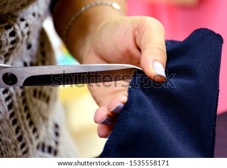 The seamstress cuts the blue fabric with the help of tailor scissors. Cutting material in a sewing workshop. Preparation for sewing clothes. Small business.