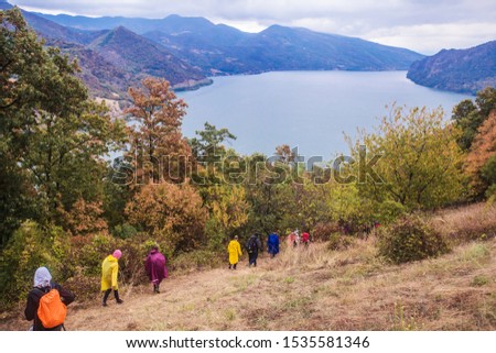 Group of active people hiking on the rural landscape. Real unrecognizable hikers. Rearview. Cloudy autumn day. View on the Danube river in the background.