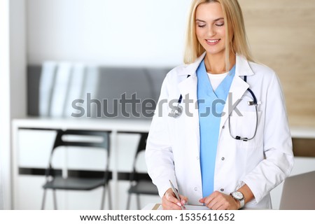 Doctor woman at work in hospital excited and happy of her profession. Blonde physician controls medication history records and exam results. Medicine and healthcare concept