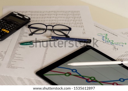 Photography of an office desk of a businessman with a tablet, a calculator, graphs, pens and glasses to see.