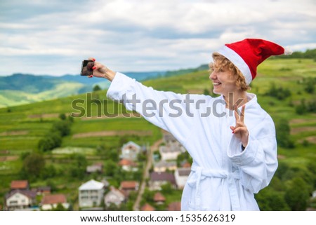 Beautiful happy woman in Santa Claus hat making selfie photo with phone