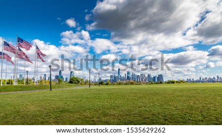 View from Liberty State Park in. New Jersey with American flags waving in the wind to the skyline of lower Manhattan at a warm day with a dramatic cloudscape in autumn.