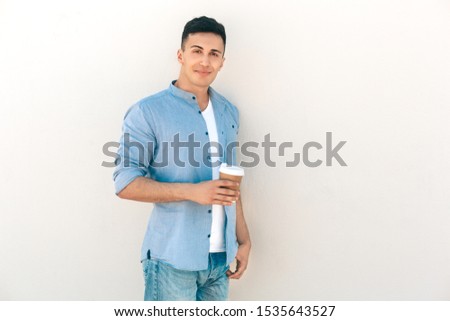Stylish young man standing outdoors isolated on white background holding disposable cup of hot coffee looking camera smiling playful
