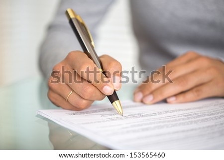 Woman at office desk signing a contract with shallow focus on signature.