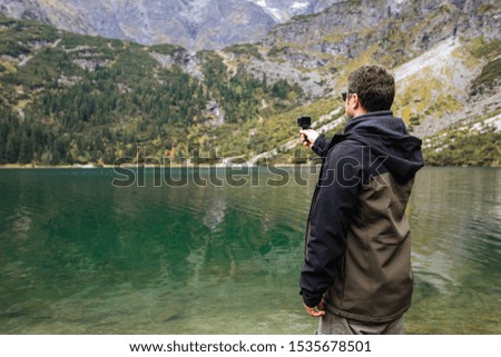 Tourist with action camera in hand. Tatra National Park, Poland. Small Mountains Lake 'Morskie Oko' In  Morning. Beautiful Scenic View.