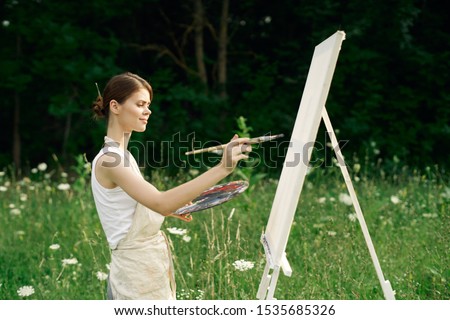 young woman with a brush in her hands an easel in nature