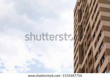 Blue cloudy sky background on one side of photo and high apartment building with beige walls on the right, exterior architecture design