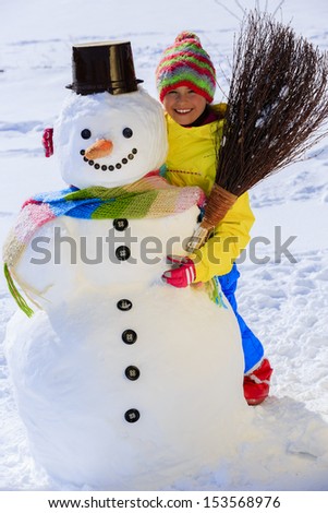 Winter fun, happy kid playing with snowman