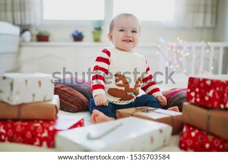 Happy little baby girl wearing warm holiday sweater opening Christmas presents on her very first Christmas. Celebrating Xmas with kids at home