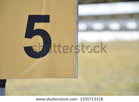 Black number 5 on a yellow plate outside on the shooting range