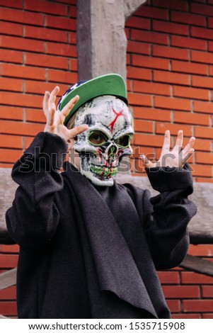 preteen boy in scary mask standing near wall outdoors on halloween 