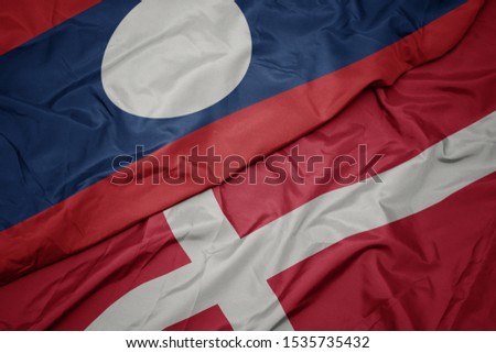waving colorful flag of denmark and national flag of laos. macro