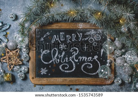 Christmas hand lettering Merry Christmas on vintage chalkboard with fir tree, golden stars, toys and lighted garland over blue texture background. Flat lay, space