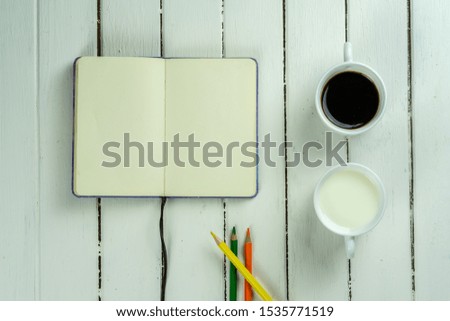 open notebook, glass of cofee and glass of milk on White wood