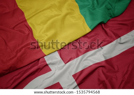 waving colorful flag of denmark and national flag of guinea. macro