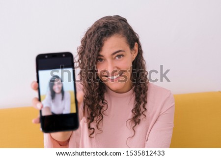 Young female with beautiful smile photographing herself for social network pictures. Single woman on social media application. Holding a smart phone with her picture profile. Focus on her face.