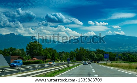 View of the road with cars, signposts and Alps mountains on the road towards the town of Annecy.Haute-Savoie in France.
