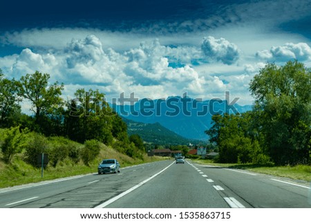 View of the road with cars, signposts and Alps mountains on the road towards the town of Annecy.Haute-Savoie in France.