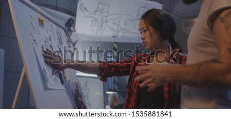 Medium shot of a male and a female designer discussing video game artwork