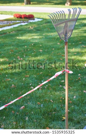 Red and white guard tape tied to a rake handle separates the cleaning area in a public park