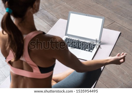 Rear back over shoulder view at fit sporty healthy calm woman sit on mat in lotus pose watching online yoga class meditate do breathing exercises on laptop computer blank white mock up screen concept Royalty-Free Stock Photo #1535954495