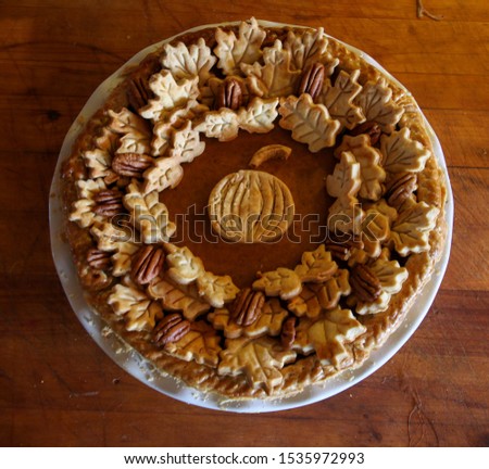 Homemade Thanksgiving Pumpkin Pie decorated with pastry leaves, pecans with a center pumpkin on a wooden board