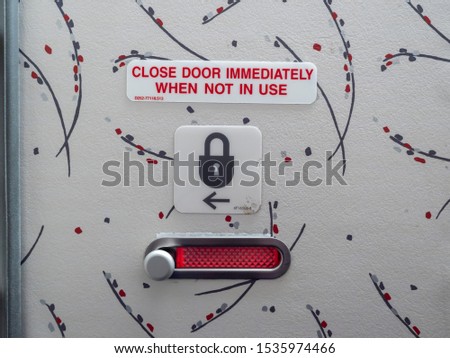 Locked airplane bathroom door seen from inside with a "close door immediately when not in use" sign and a picture of a lock with an arrow. The red window indicates the bathroom is occupied