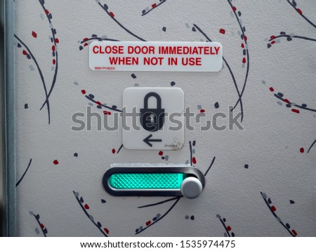 View from inside an unlocked airplane bathroom with a "close door immediately when not in use" sign and a picture of a lock with an arrow to show how to secure the door. Green glow shows door is open