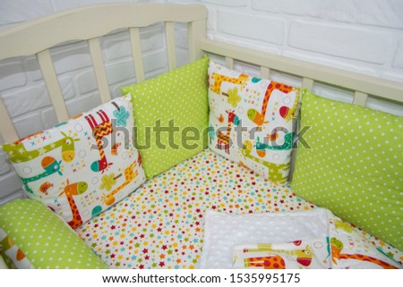 Set of bed linen in the crib. Textiles for newborn green and white with a picture of giraffes and a pattern of circles. Pillows on the sides of the crib, blanket, envelope for discharge, rollers.