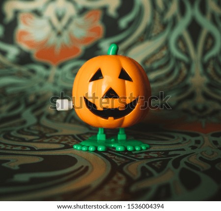 A photograph of a pumpkin wind up toy on a floral backdrop